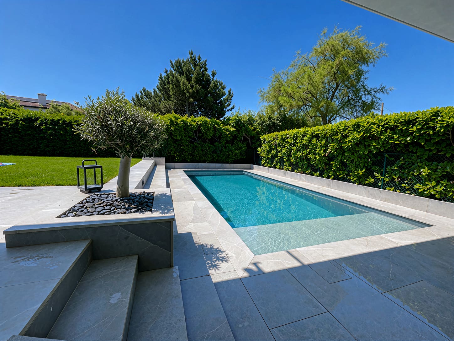 Piscine traditionnelle bordée de pierre claire et de graminées
